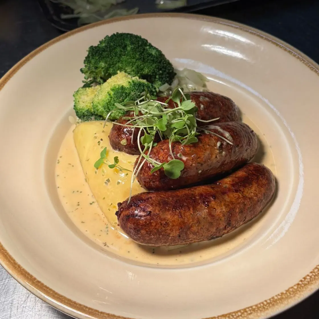 Three Cumberland sausages on mashed potato with broccoli and a cider and sage cream sauce
