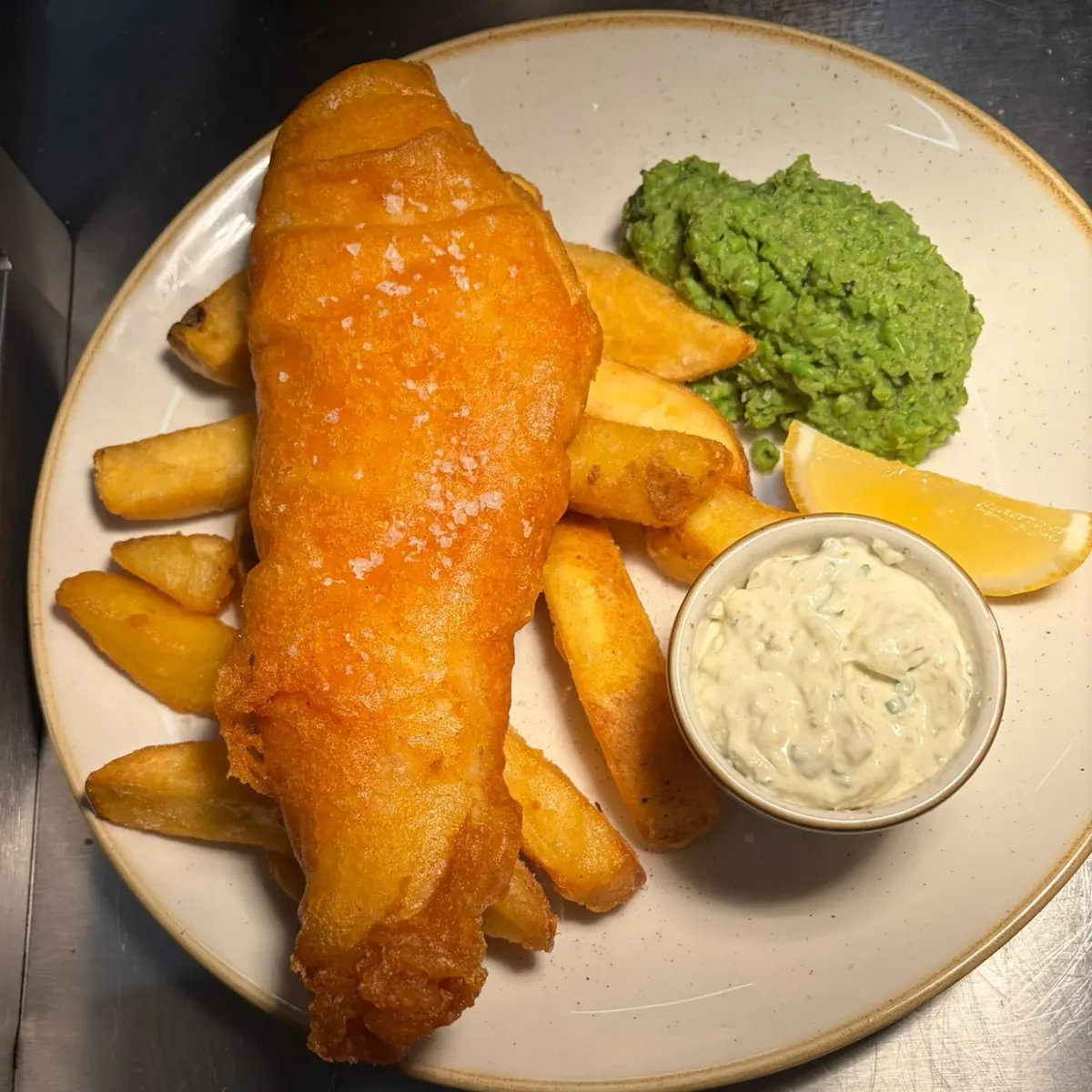 Battered fish with chunky chips, mushy peas, a wedge of lemon and a pot of tartare sauce