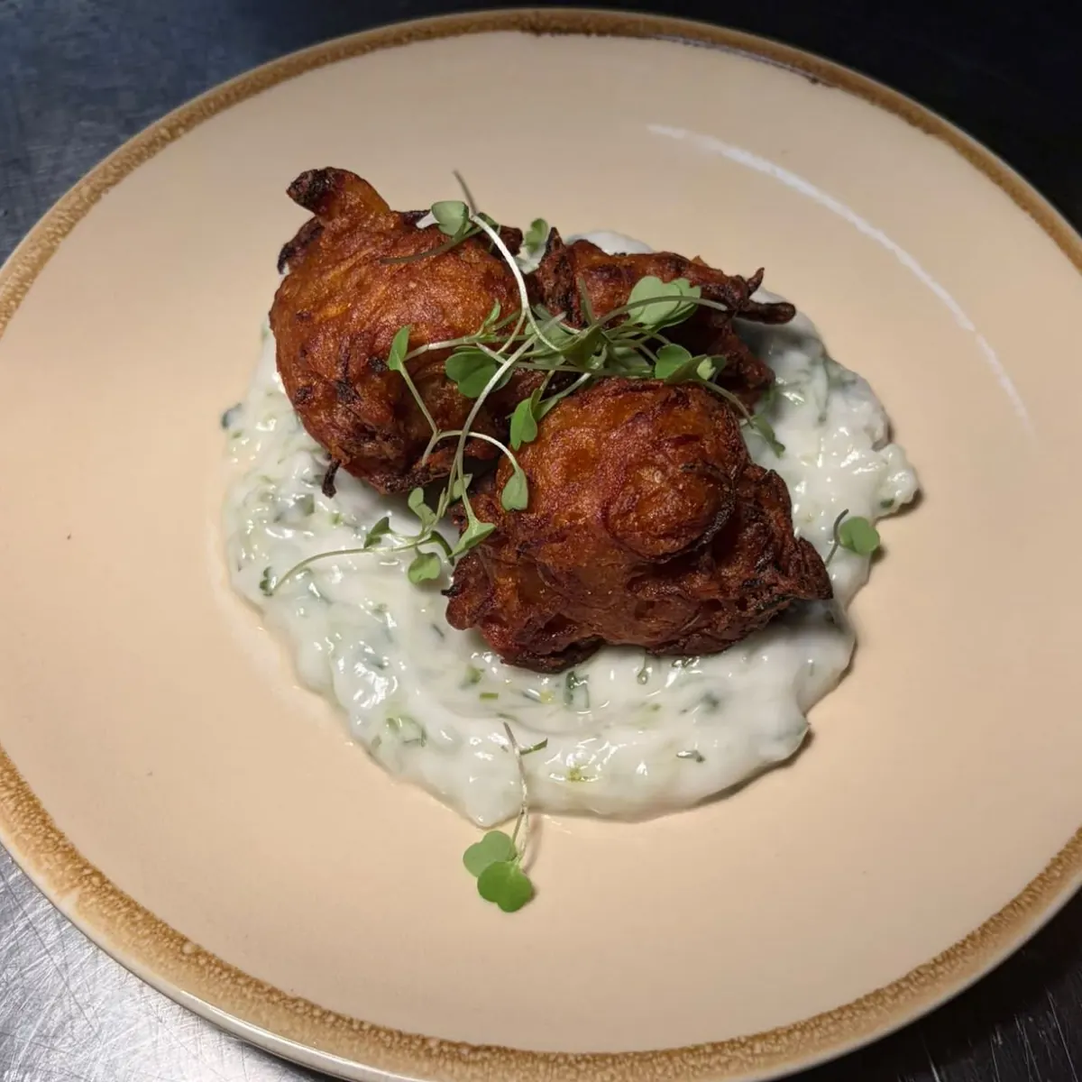 Three onion bhajis with micro herbs on a bed of coconut yoghurt raita