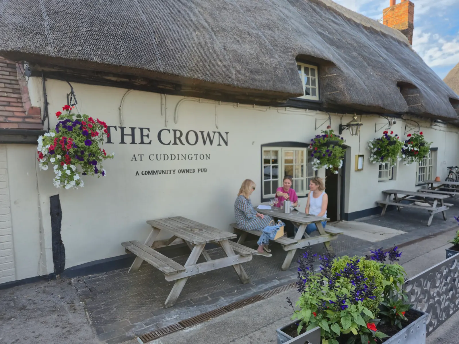Three people sharing a bottle of wine at a picnic table outside the front of The Crown