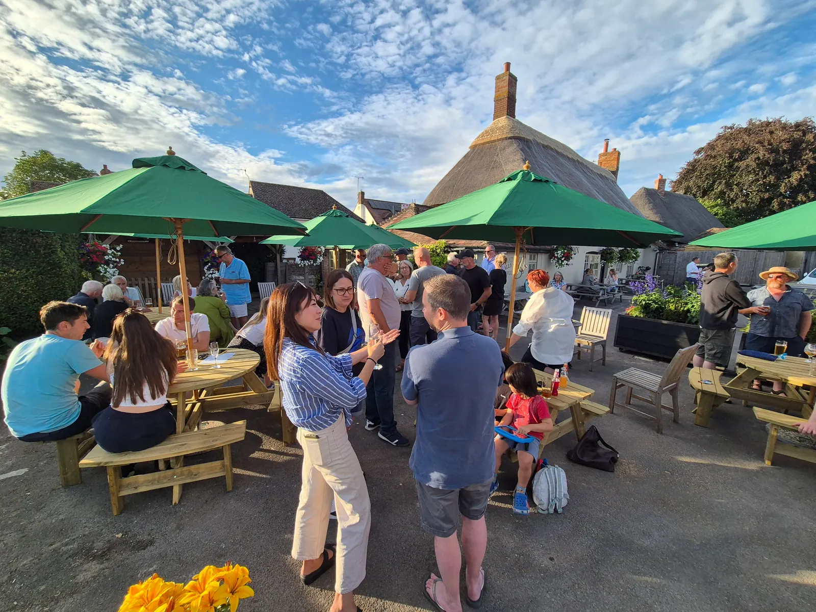 A busy garden at The Crown, green parasols and picnic tables beneath the thatched roof
