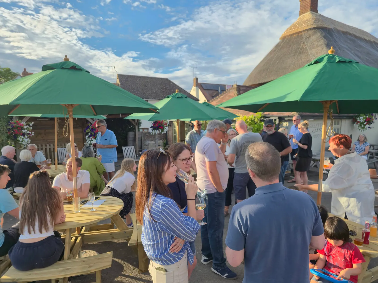 A large group of customers with drinks in the garden at The Crown on a summer evening