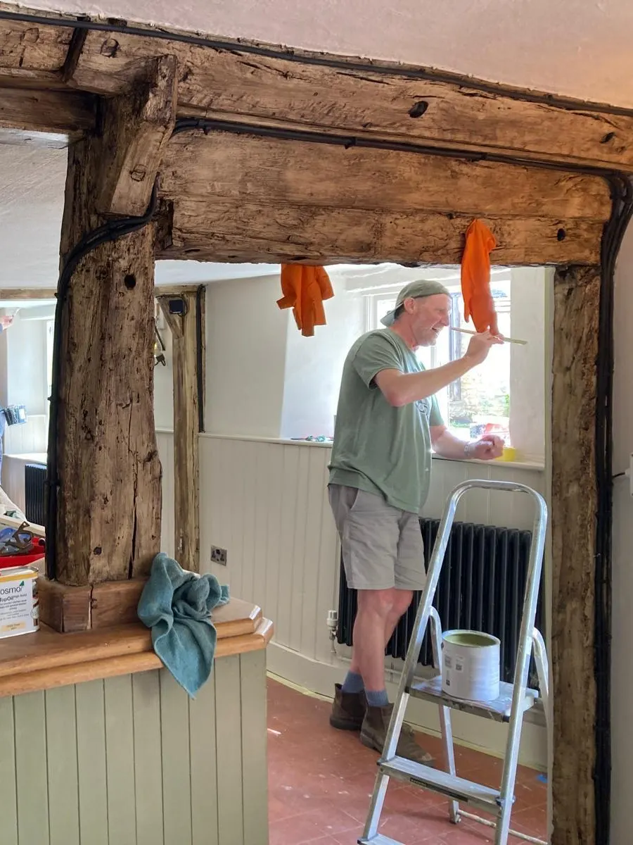 A volunteer painting the wall beneath the pub's original oak beams, paint tin on a stepladder