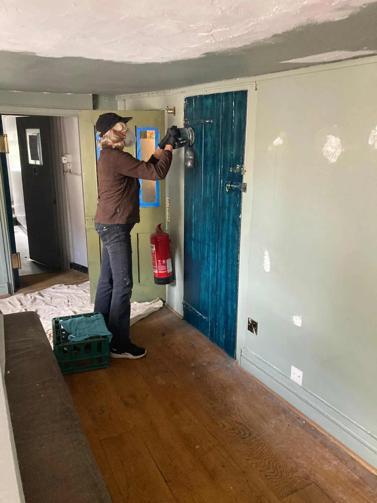 A volunteer in a dust mask sanding an old painted door back with a power sander