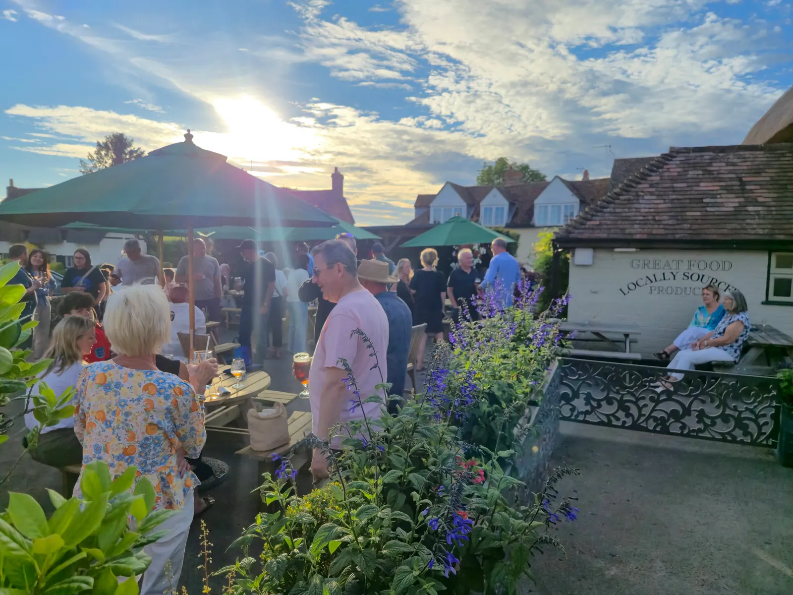 The garden at The Crown on a summer evening, full of people with drinks as the sun sets behind the parasols