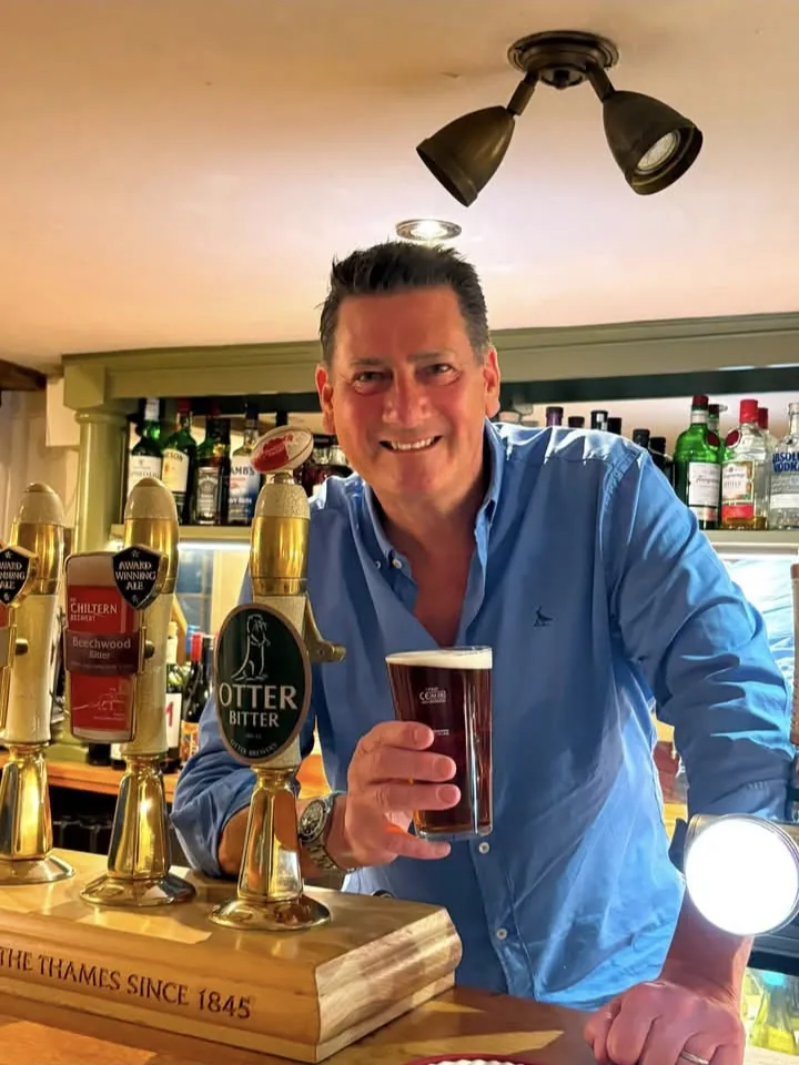 Tony Hadley standing at the bar of The Crown, raising a pint of Otter Bitter